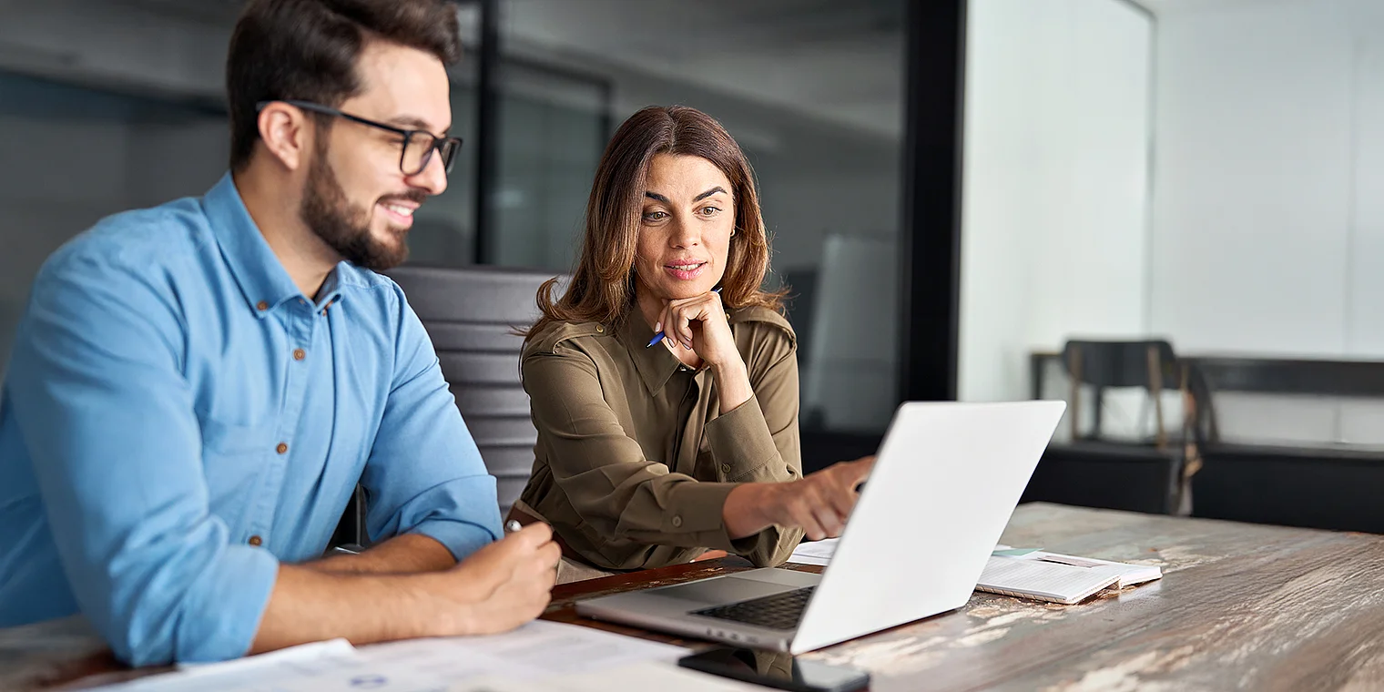 Zwei Personen arbeiten konzentriert gemeinsam an einem digitalen Interface, das barrierefreie Weblösungen symbolisiert und die Leistungen zur Barrierefreiheit der Webagentur Netigo visualisiert; der Bildhintergrund zeigt Elemente, die nutzerfreundliche, zugängliche Gestaltung und inklusive digitale Anwendungen unterstreichen.