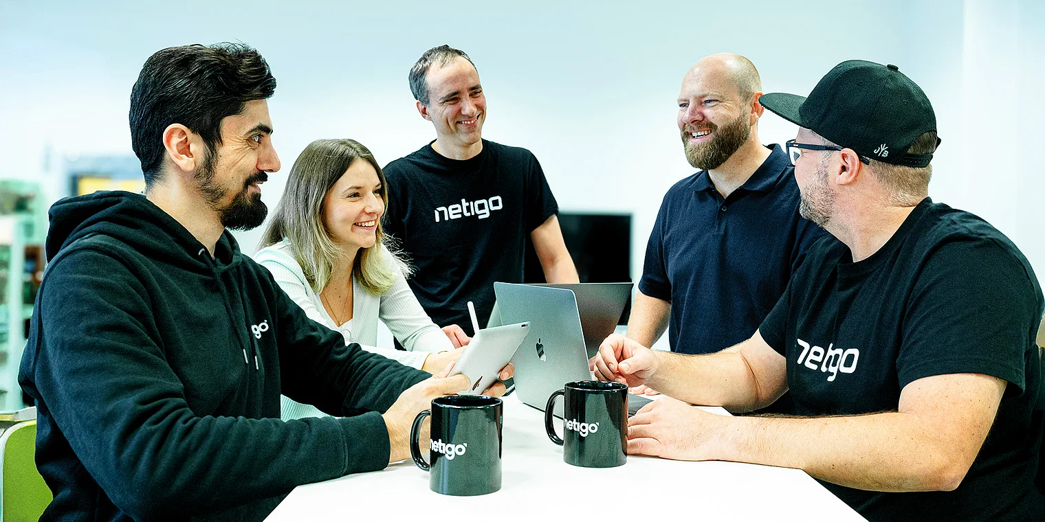 Melissa, Tobias Bühne, Martin Widemann, Claudio und Omar von der Netigo GmbH stehen bzw. sitzen gemeinsam in einer Agenturumgebung und repräsentieren das Team der Webagentur in Düsseldorf; das Bild vermittelt Teamwork, Professionalität und Zusammenarbeit in einem modernen Büro.